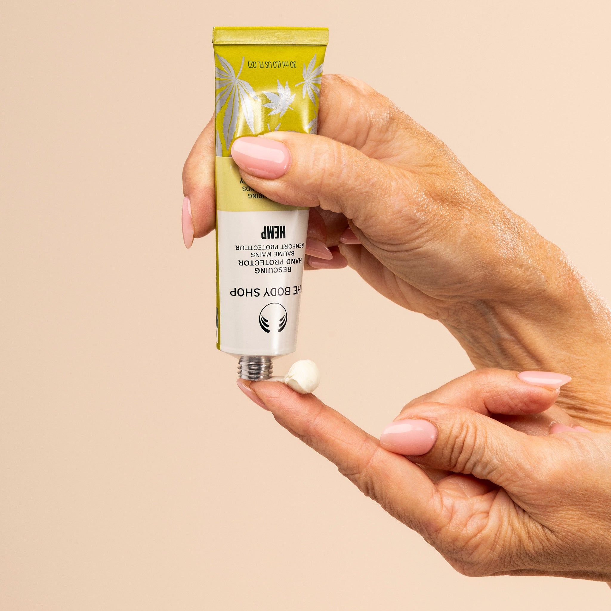Hand holding a tube of hemp hand protector against a beige background